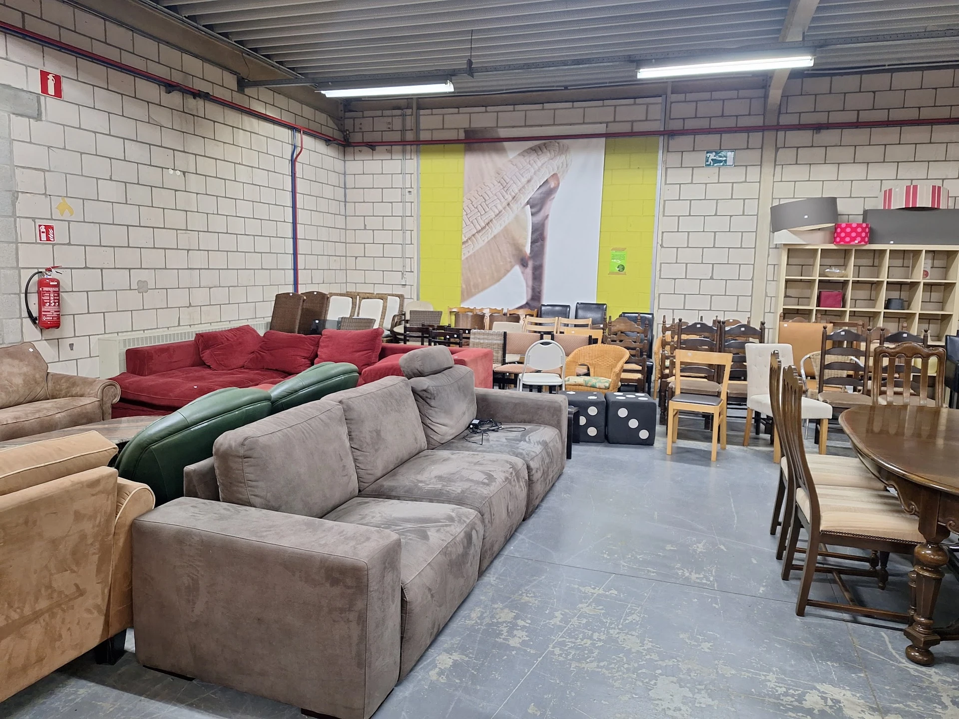 Winkelvloer met gebruikte meubels: grijze en rode banken, houten stoelen, tafels en stellingen met huishoudartikelen
