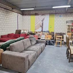 Winkelvloer met gebruikte meubels: grijze en rode banken, houten stoelen, tafels en stellingen met huishoudartikelen