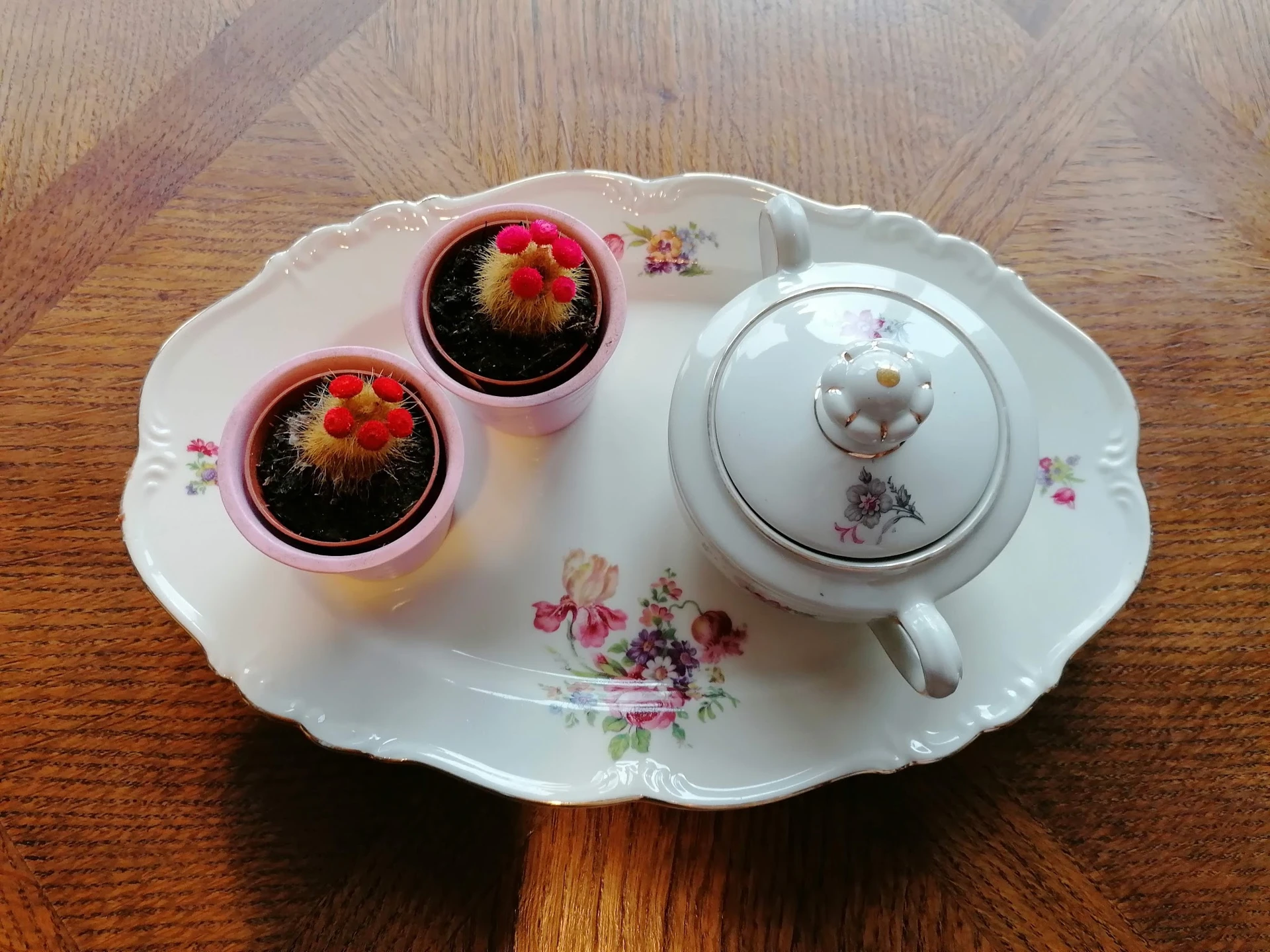 Witte porseleinen serveerschaal met bloemmotief, twee roze potjes met cactussen en een theepot.