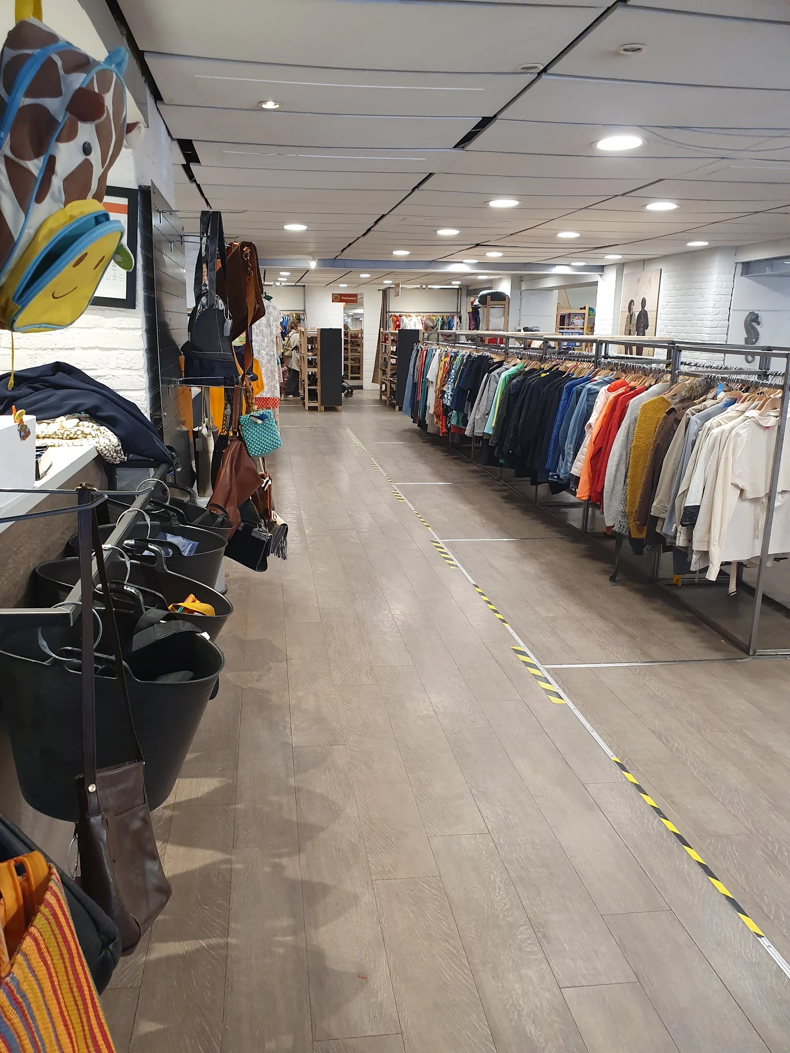 Winkelinterieur met kledingrekken vol tweedehands kleding in verschillende kleuren langs de wanden