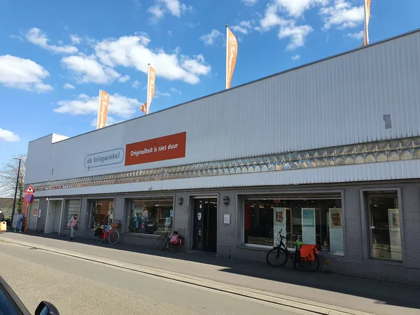 Gevel van kringloopwinkel met grote ramen, ingang en uitgestalde fietsen voor de deur