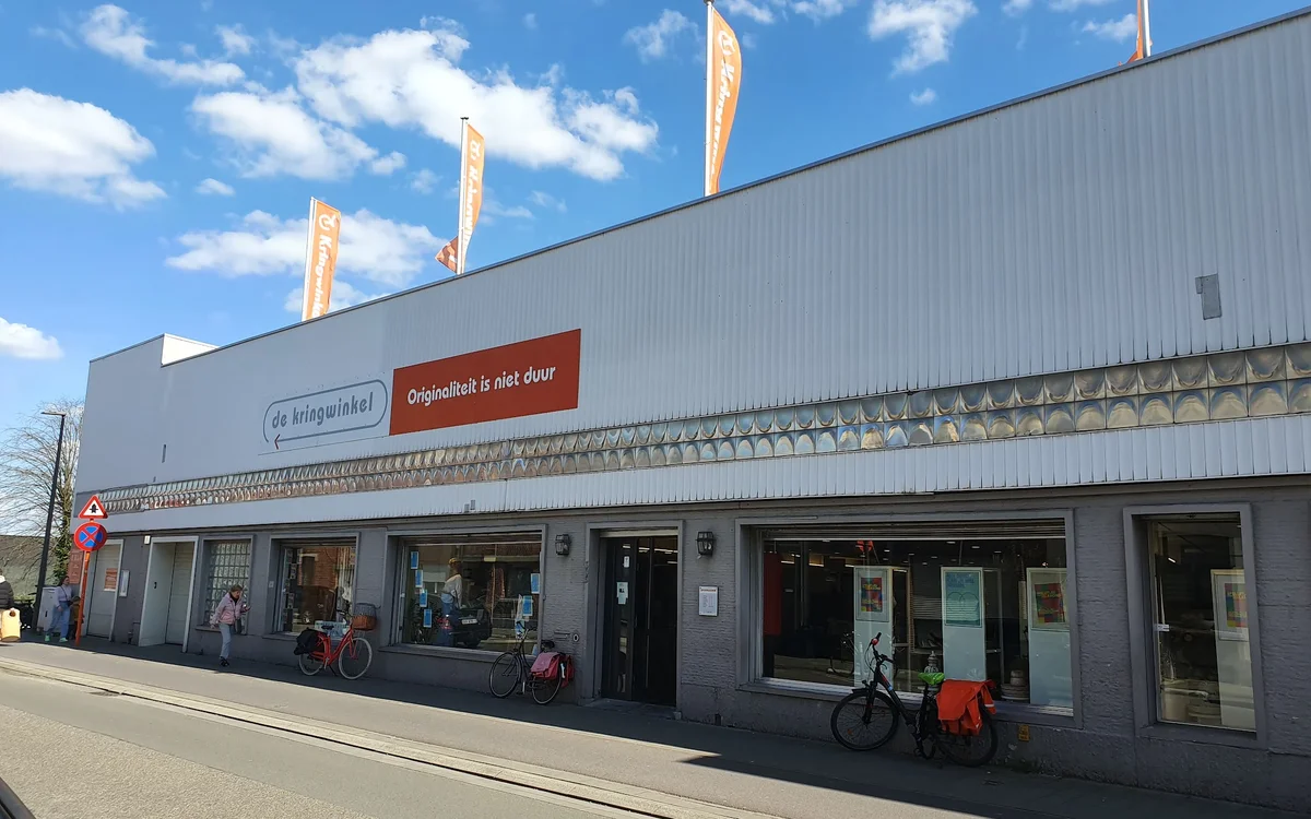 Gevel van kringloopwinkel met grote ramen, ingang en uitgestalde fietsen voor de deur