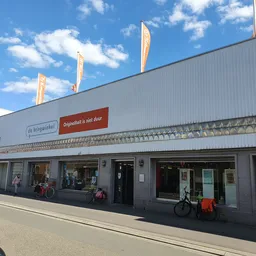Gevel van kringloopwinkel met grote ramen, ingang en uitgestalde fietsen voor de deur