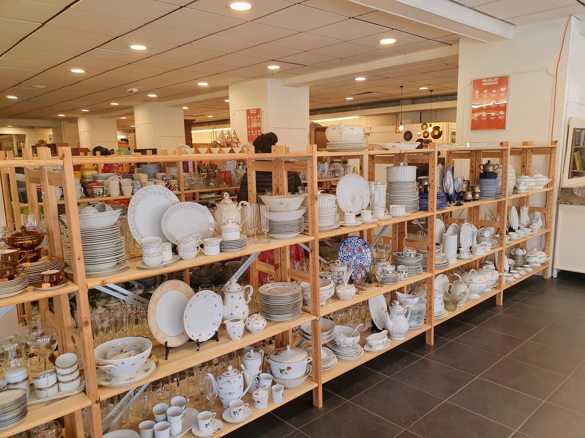 Houten stellingen vol met serviesgoed, borden, kopjes en ander keramiek in een kringloopwinkel