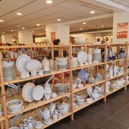 Houten stellingen vol met serviesgoed, borden, kopjes en ander keramiek in een kringloopwinkel