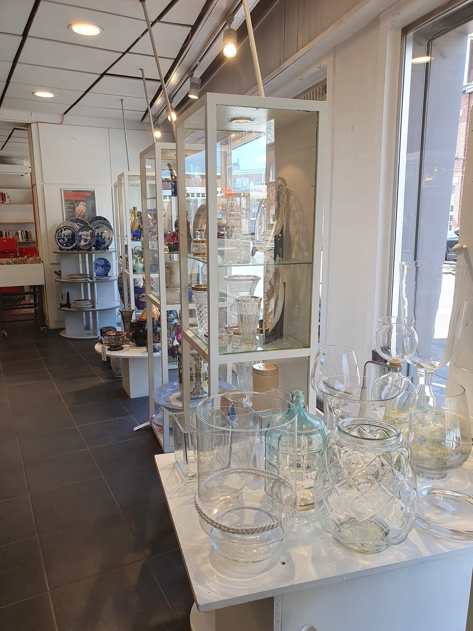 Glazen vitrinekasten met kristalglas, glazen servies en decoratieve voorwerpen in een kringloopwinkel