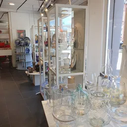 Glazen vitrinekasten met kristalglas, glazen servies en decoratieve voorwerpen in een kringloopwinkel