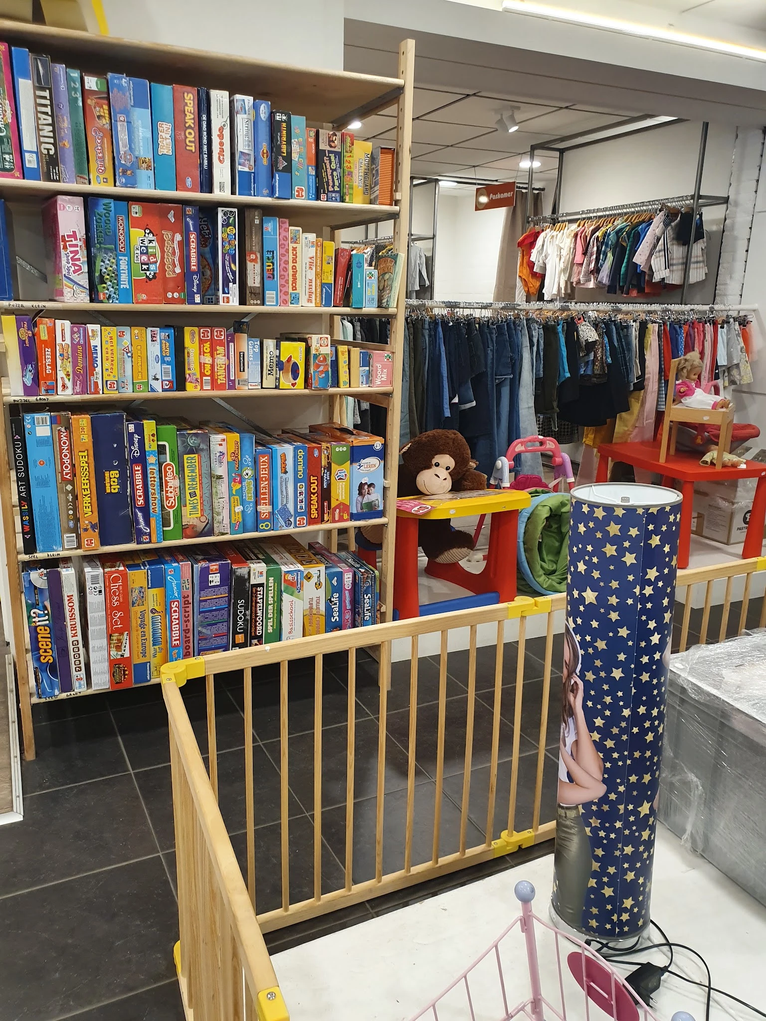 Winkelbinnenruimte met boekenrekken links, kinderkleding op hangers rechts, speelgoed en accessoires in het midden