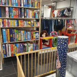 Winkelbinnenruimte met boekenrekken links, kinderkleding op hangers rechts, speelgoed en accessoires in het midden