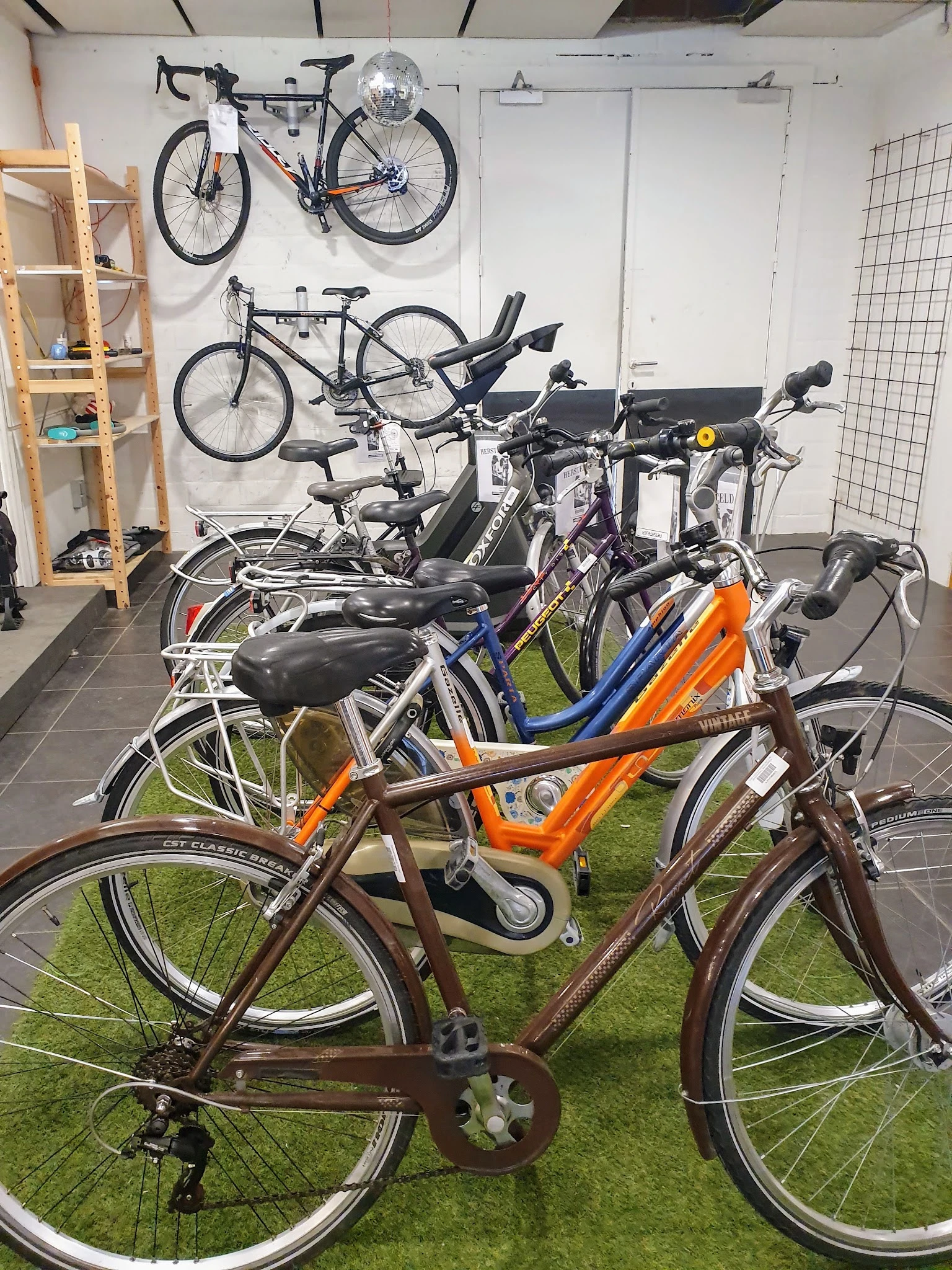 Verzameling tweedehands fietsen in verschillende kleuren en modellen op een groen oppervlak in de winkel