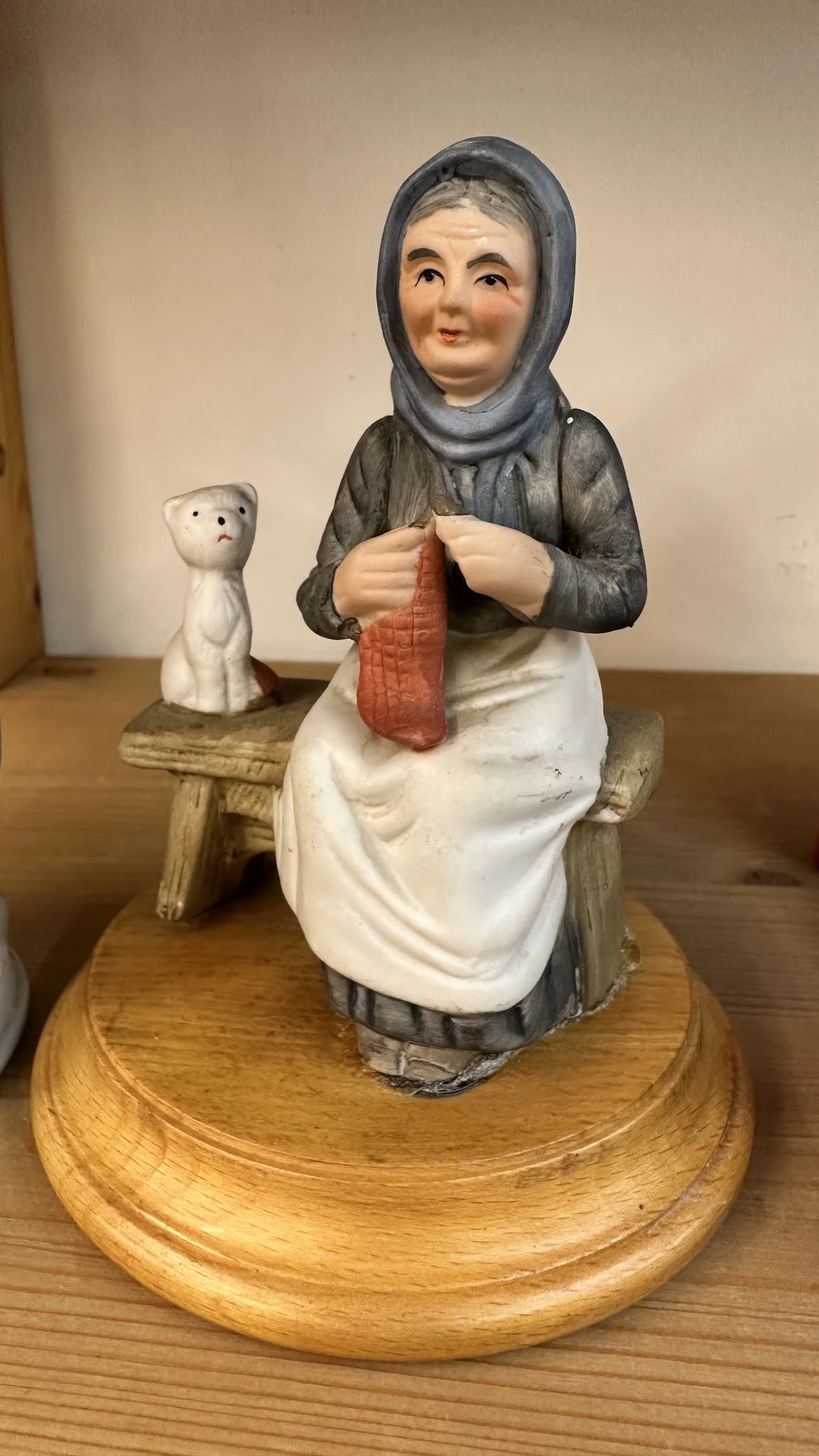 Keramisch beeldje van een vrouw in traditionele kledij die aan textiel werkt, met een klein wit katje op de achtergrond