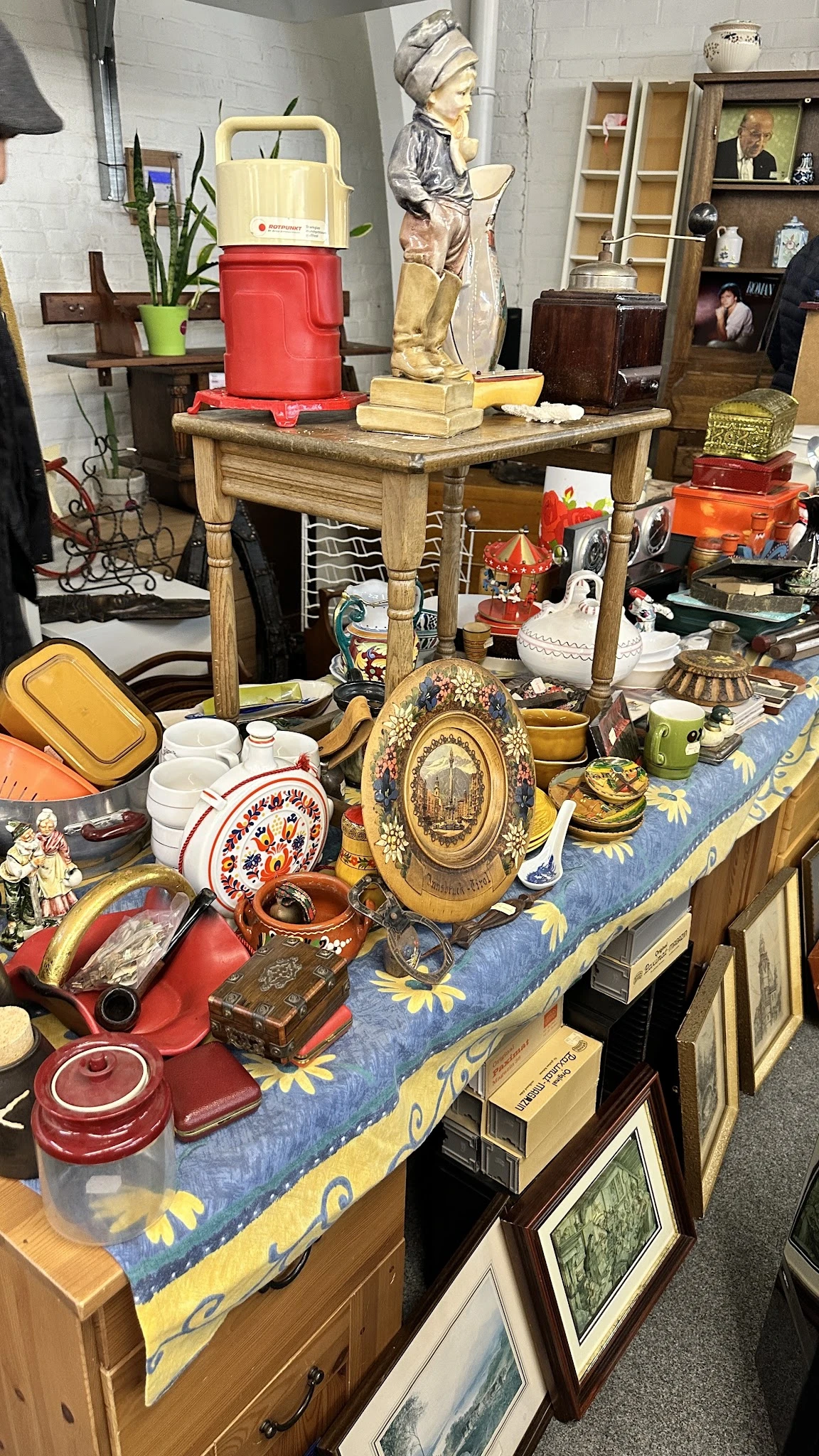 Uitgestalde tweede­hands huishoudarti­kelen: decoratief bord­werk, servies, kandelaars en ander vintage huisraad op tafel.