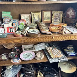 Houten schappen volgestapeld met vintage decoratieve items, borden, lijsten en antieke spullen