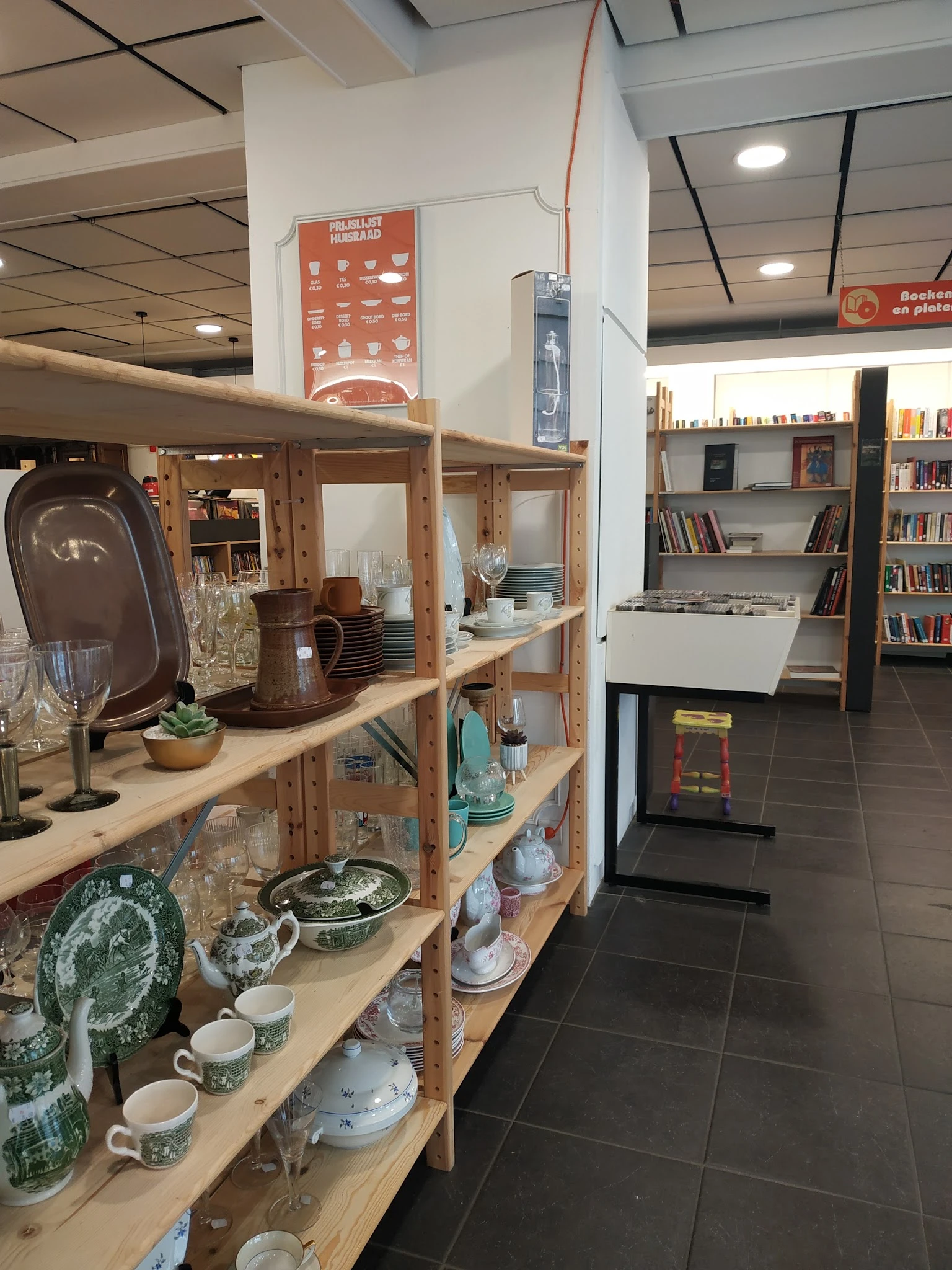 Houten stellingkast met huishoudelijke artikelen, servies, glazen en decoratieve voorwerpen in een kringloopwinkel