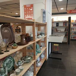 Houten stellingkast met huishoudelijke artikelen, servies, glazen en decoratieve voorwerpen in een kringloopwinkel