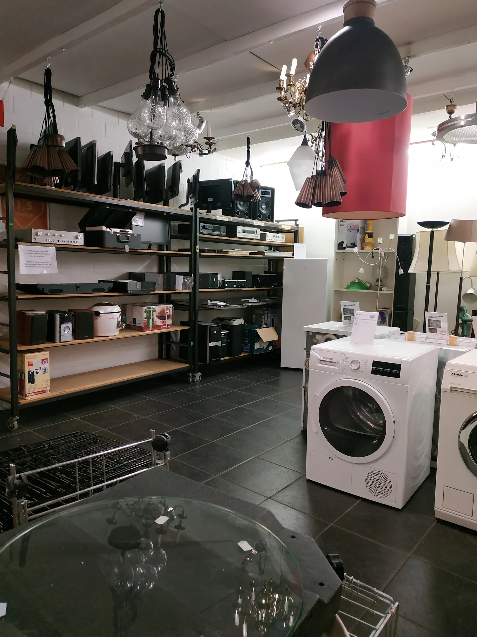 Winkelvloer met witgoedsectie: wasmachines en drogers, stellingen met huishoudartikelen en een rode hanglamp