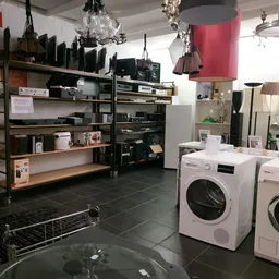 Winkelvloer met witgoedsectie: wasmachines en drogers, stellingen met huishoudartikelen en een rode hanglamp