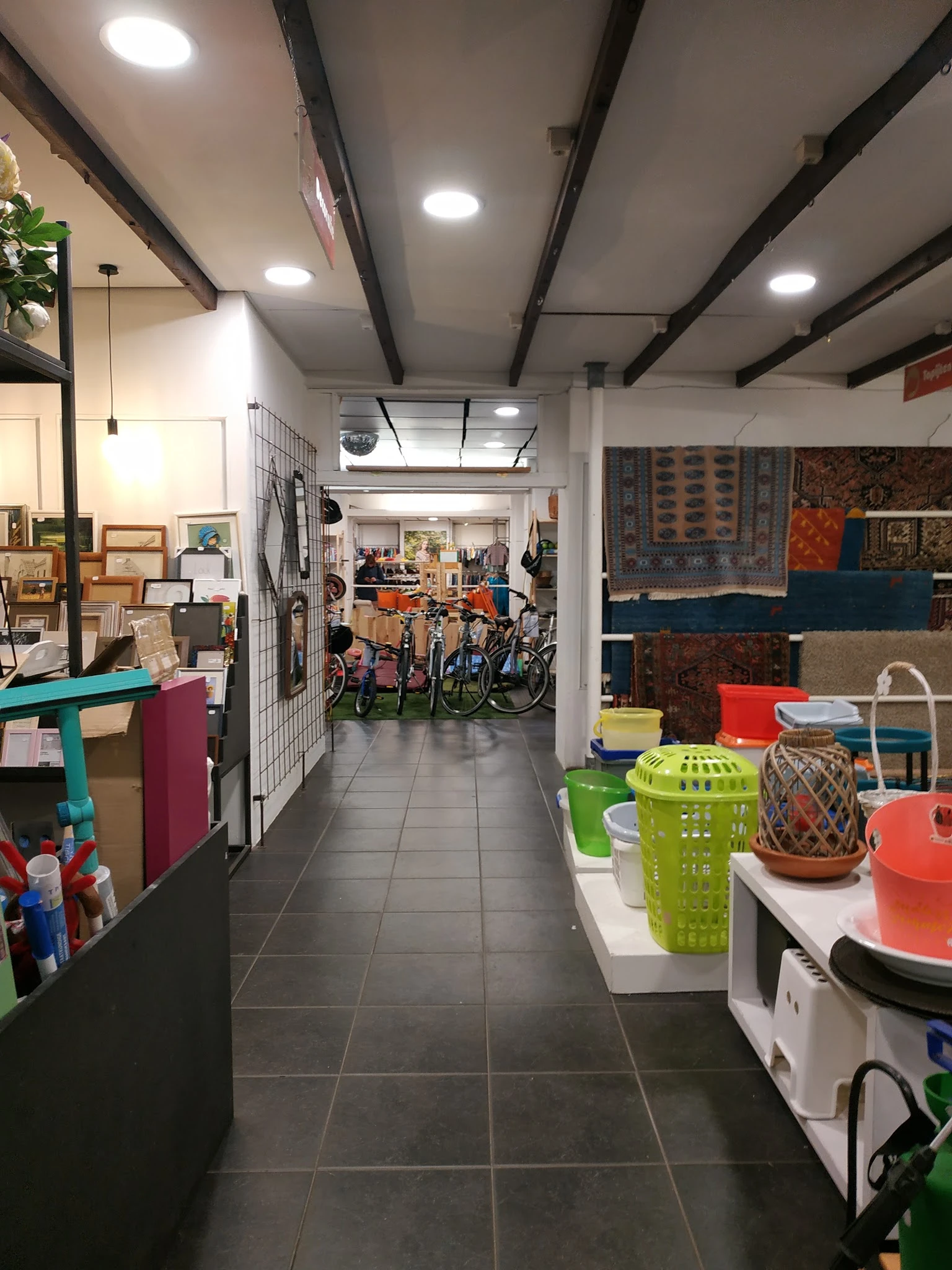 Winkelinterieur met diverse spullen: links rekken met kledingarikelen en huishoudspullen, rechts kleurige plastic manden en r