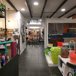 Winkelinterieur met diverse spullen: links rekken met kledingarikelen en huishoudspullen, rechts kleurige plastic manden en r