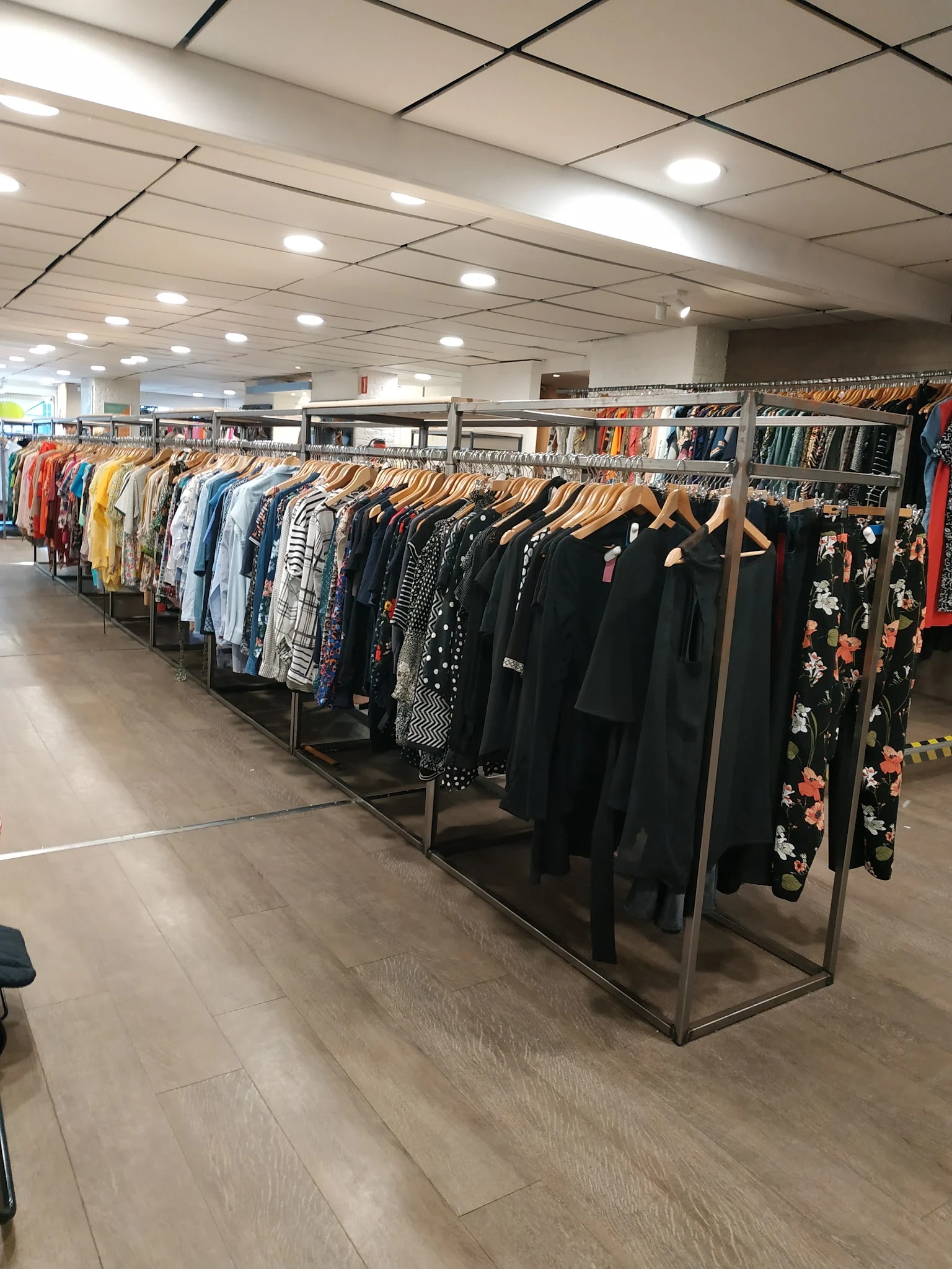 Rekken met tweedehands kleding op houten hangers, veel zwarte en gekleurde items