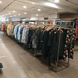 Rekken met tweedehands kleding op houten hangers, veel zwarte en gekleurde items
