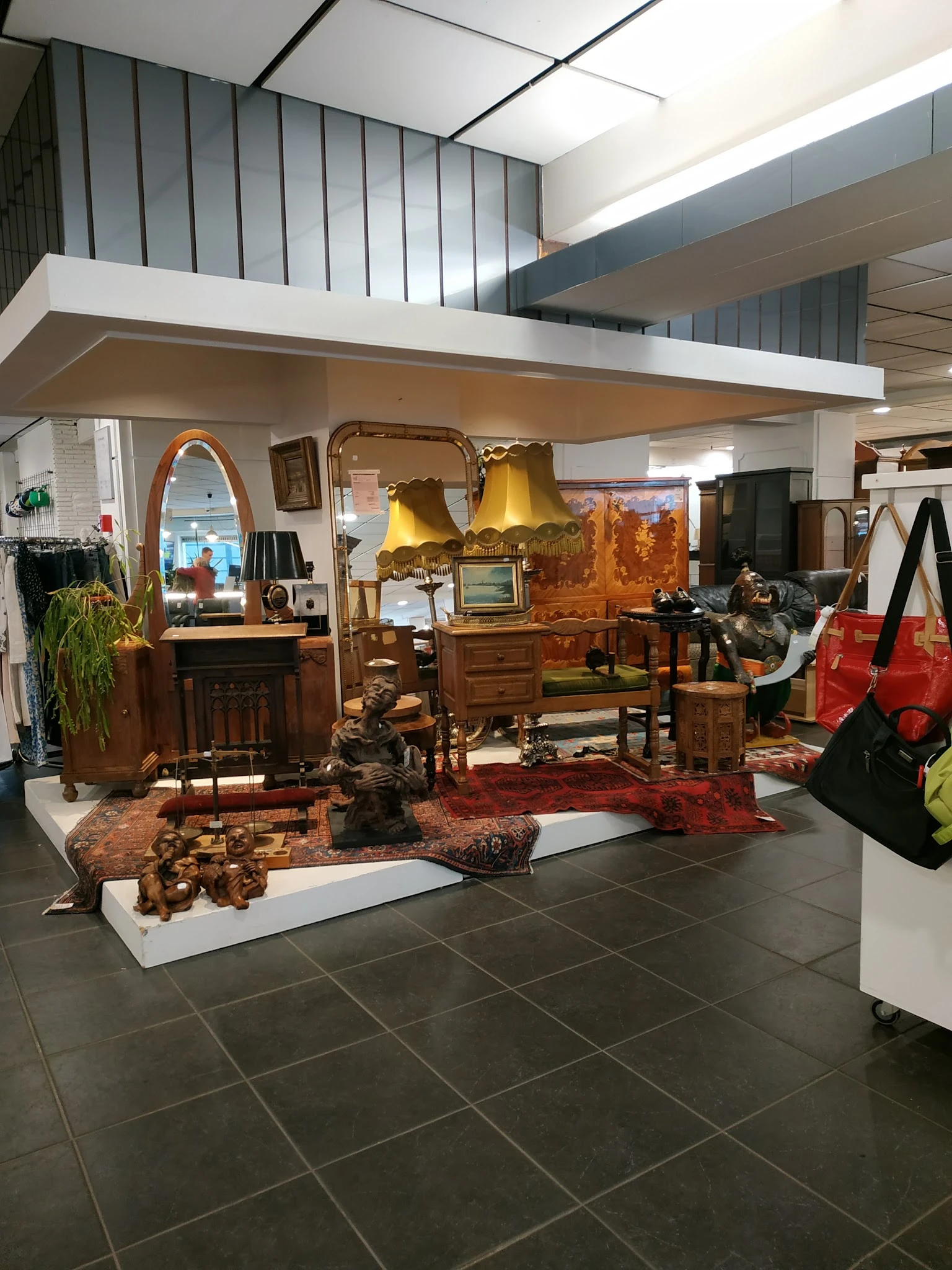 Uitgestalde meubels en huishoudartikelen in een kringloopwinkel, waaronder houten kasten, lampen, een tapijt en diverse decor