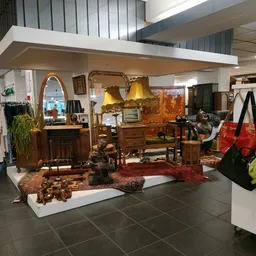 Uitgestalde meubels en huishoudartikelen in een kringloopwinkel, waaronder houten kasten, lampen, een tapijt en diverse decor