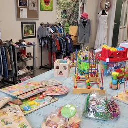 Kinderspeelgoed en bababoeken uitgestald op een tafel, met kledingrekken op de achtergrond