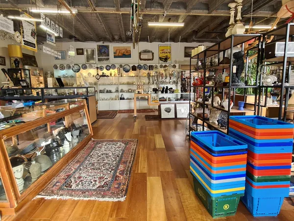 Winkelvloer met houten vloer, verschillende rekken met spullen, verzamelaars items aan de muur en gekleurde plastic kratten o