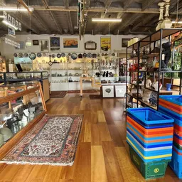 Winkelvloer met houten vloer, verschillende rekken met spullen, verzamelaars items aan de muur en gekleurde plastic kratten o