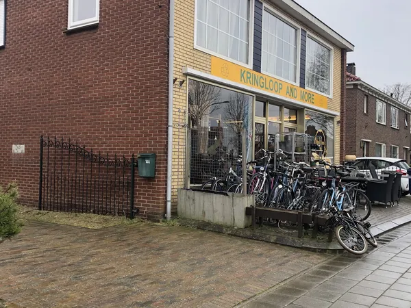 Voorkant van kringloopwinkel met gele luifel, grote ramen en fietsen op het terras