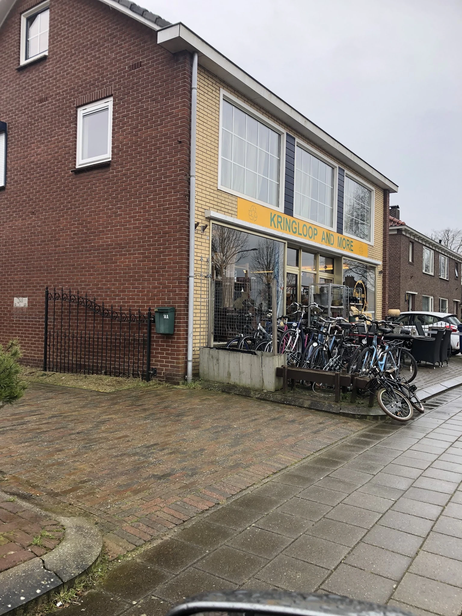 Voorkant van kringloopwinkel met gele luifel, grote ramen en fietsen op het terras