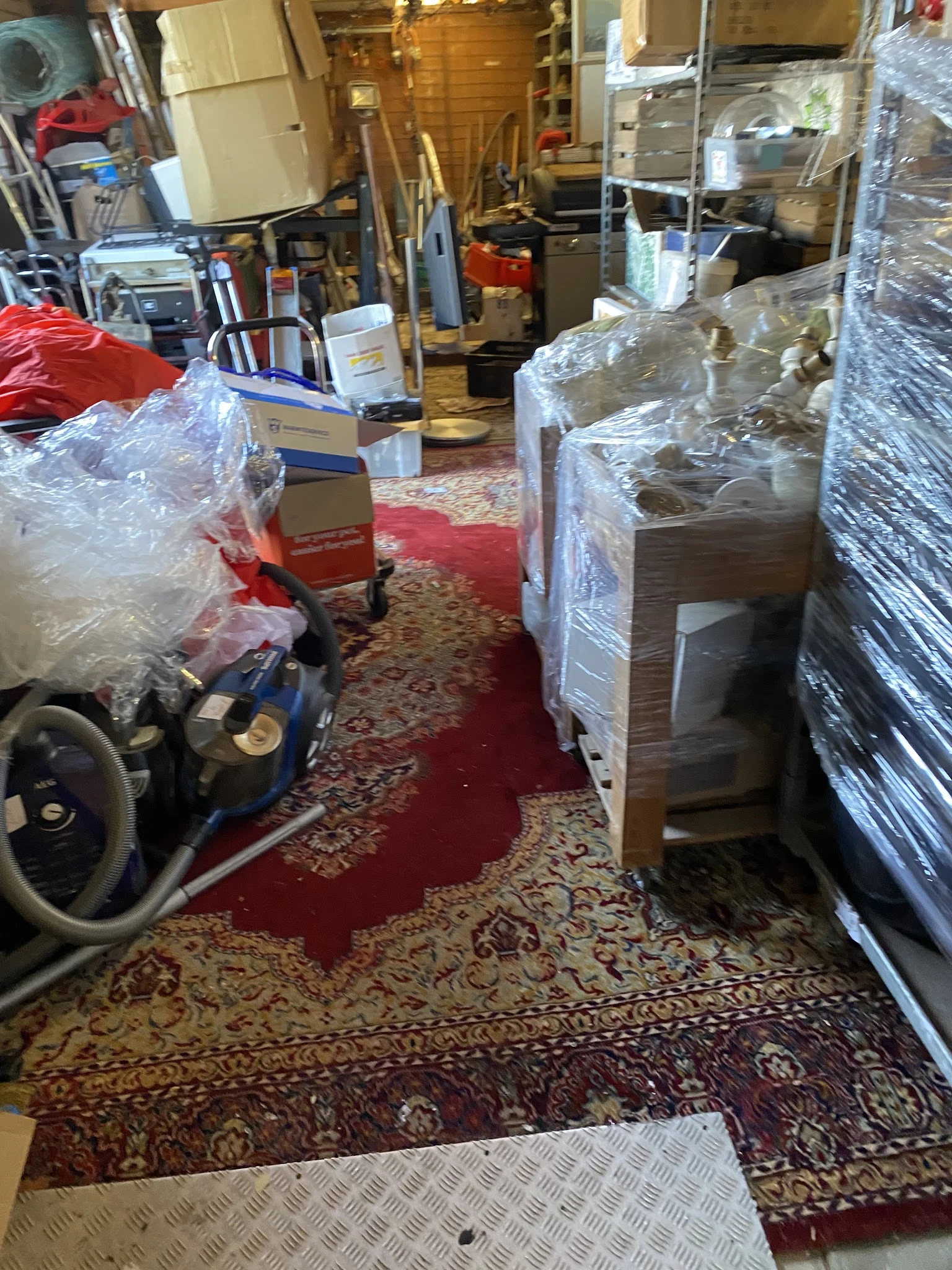 Winkelbinnenkant met in plastic verpakte meubels, werktuigen en andere spullen tussen rode en gemusterde vloerbedekking