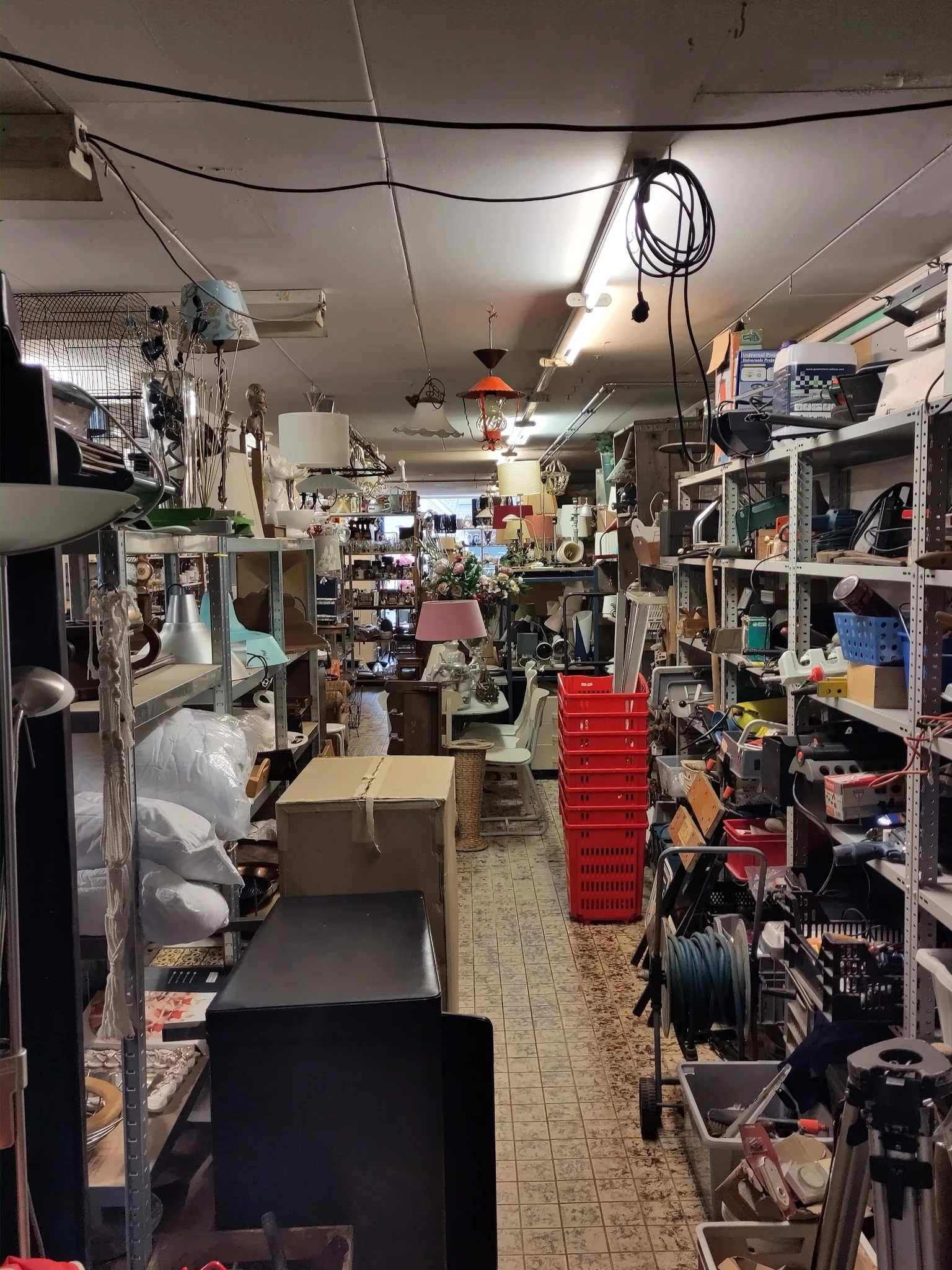 Winkelvloer van kringloopwinkel met stellingen, dozen en uiteenlopend aanbod aan tweedehands artikelen