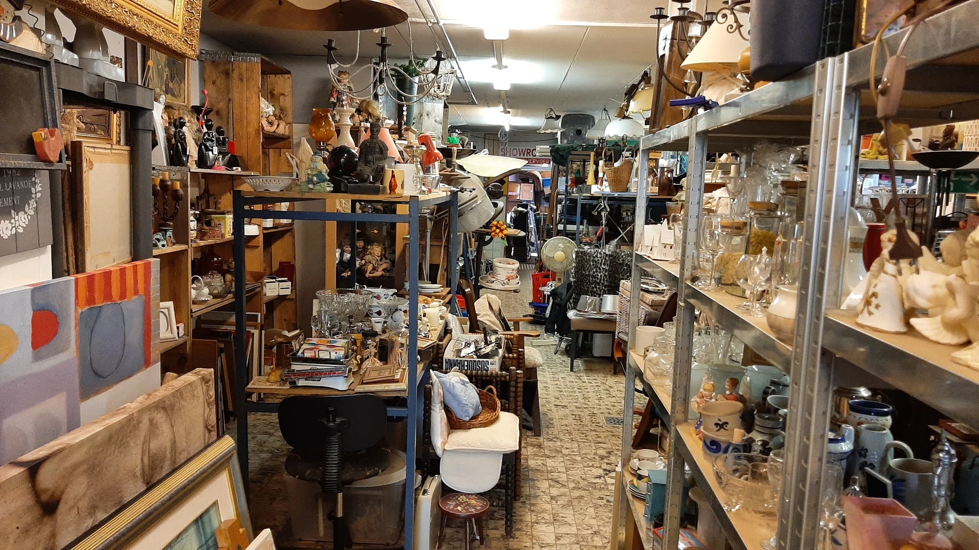 Overzicht van kringloopwinkel met stellingen, kasten en diverse tweedehands artikelen langs de winkelgang