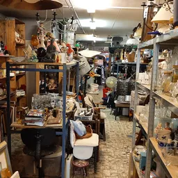 Overzicht van kringloopwinkel met stellingen, kasten en diverse tweedehands artikelen langs de winkelgang
