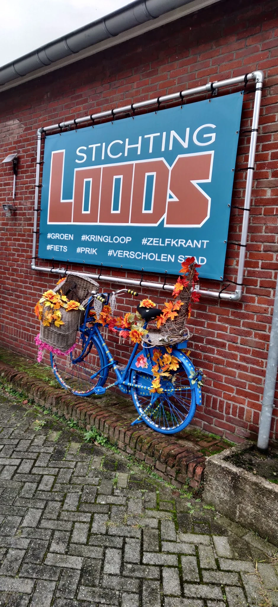 Blauwe fiets versierd met bloemen tegen rode bakstenen gevel met blauw bord