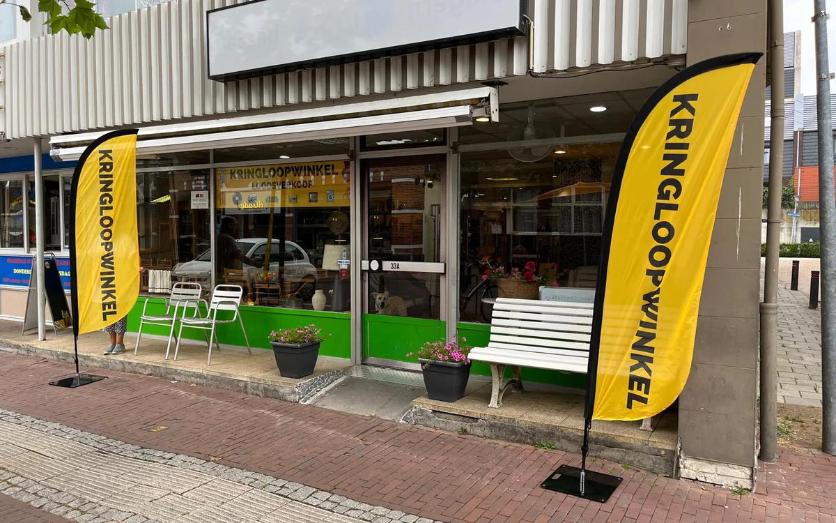 Winkelgevel met groene onderkant, gele vlaggen en zithoeken met witte stoelen en bankjes.