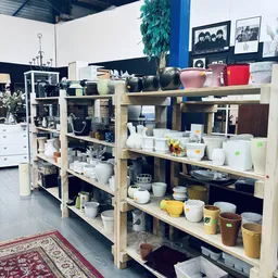 Houten stellingen met diverse keramische potten, schalen, servies en huishoudartikelen in verschillende kleuren en formaten.