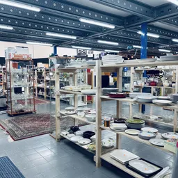 Uitgestalde servies en borden op houten stellingen in de kringloopwinkel