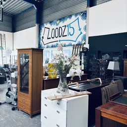 Winkelvloer met houten vitrinekast, witte ladeblok, vaas met bloemen en diverse meubels tegen donkerblauwe wand