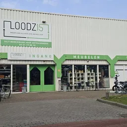 Groene winkelpui van kringloopwinkel met etalage, fietsen voor de deur en parkeerterrein