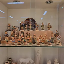 Vitrinekast met verzameling houten beeldjes en decoratieve figuren, gerangschikt op twee niveaus met spotverlichting