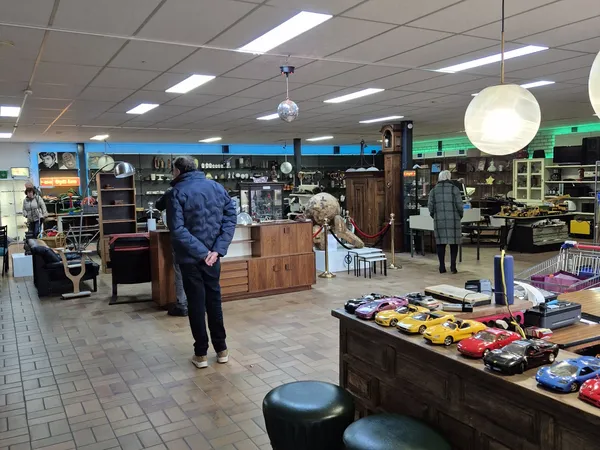 Winkelvloer van kringloopwinkel met diverse meubels, speelgoed en spullen uitgestald op tafels en stellingen