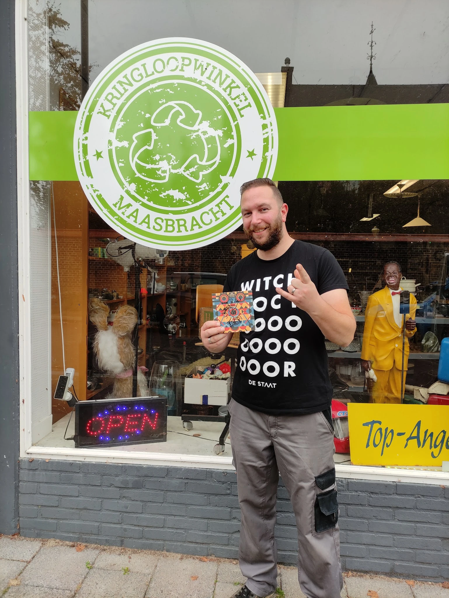 Man in zwart shirt houdt speelgoed vast en geeft duim omhoog voor de winkel