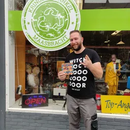 Man in zwart shirt houdt speelgoed vast en geeft duim omhoog voor de winkel