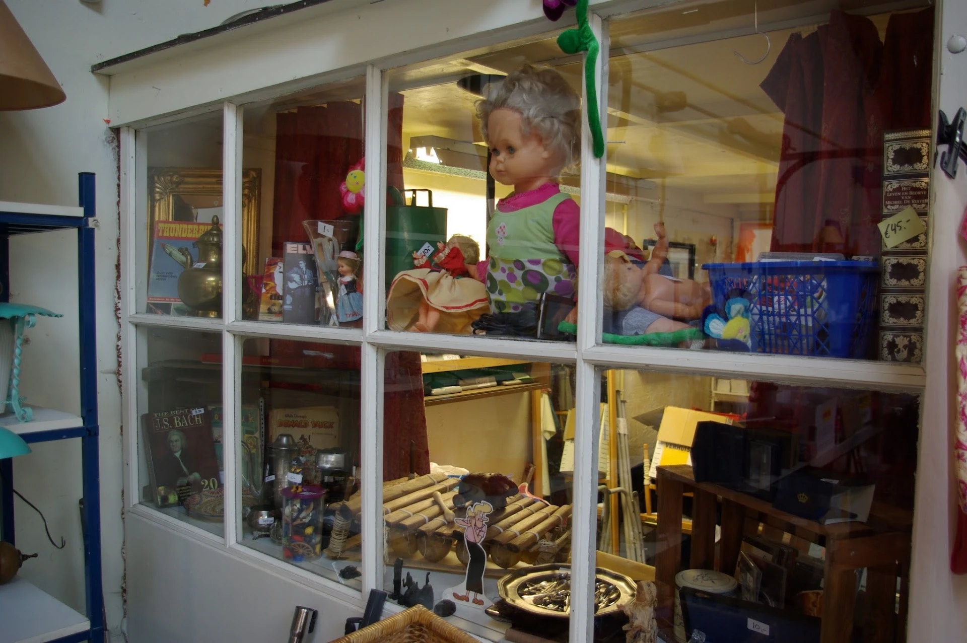 Binnenkant van kringloopwinkel met vitrinekasten en uiteenlopende spullen op planken en rekken