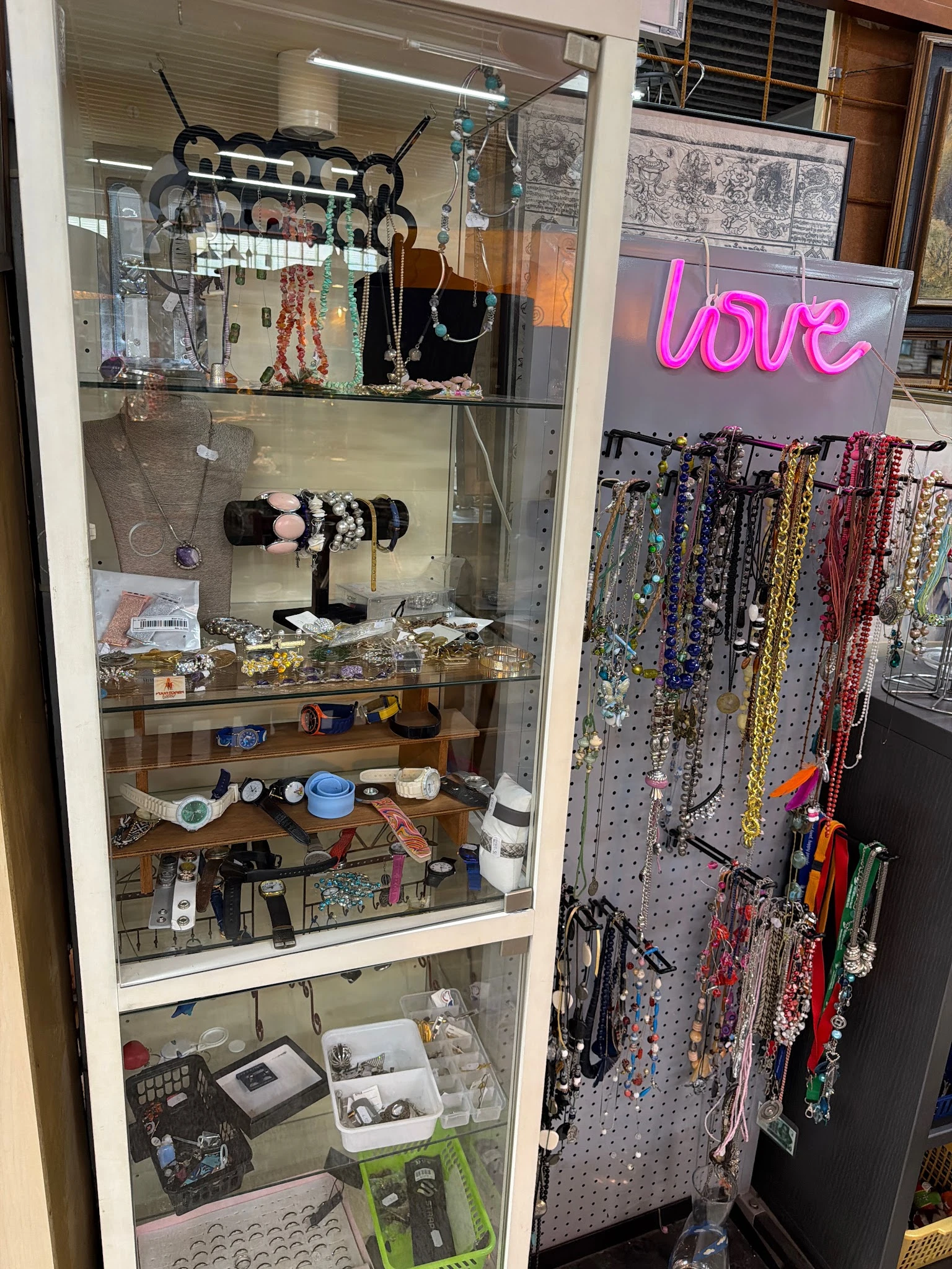 Glazen vitrine met sieraden, armbanden en accessoires; pegboard met kleurige kralen en kettingen op de achtergrond
