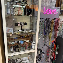 Glazen vitrine met sieraden, armbanden en accessoires; pegboard met kleurige kralen en kettingen op de achtergrond