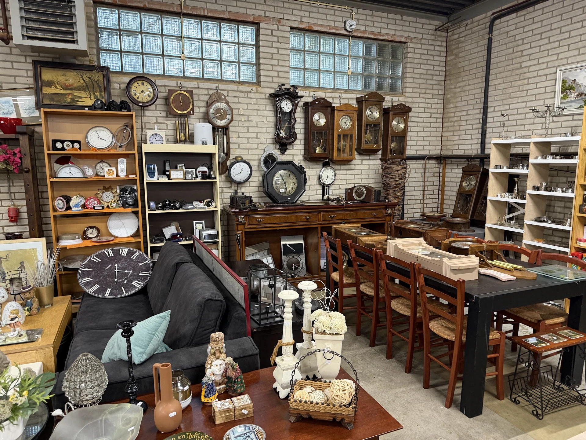 Interieur van kringloopwinkel met klokken, servies, meubels en verzamelobjecten op stellingen en tafels